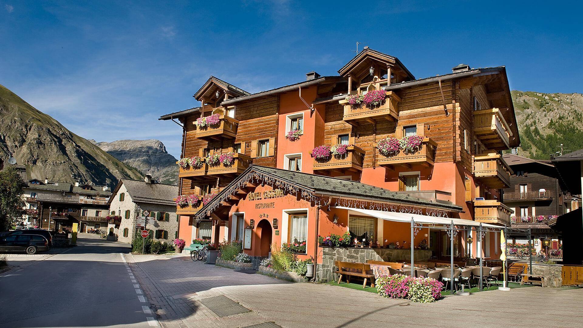 La facciata dell’Hotel Cassana in estate, con i balconi in legno fioriti e le montagne sullo sfondo
