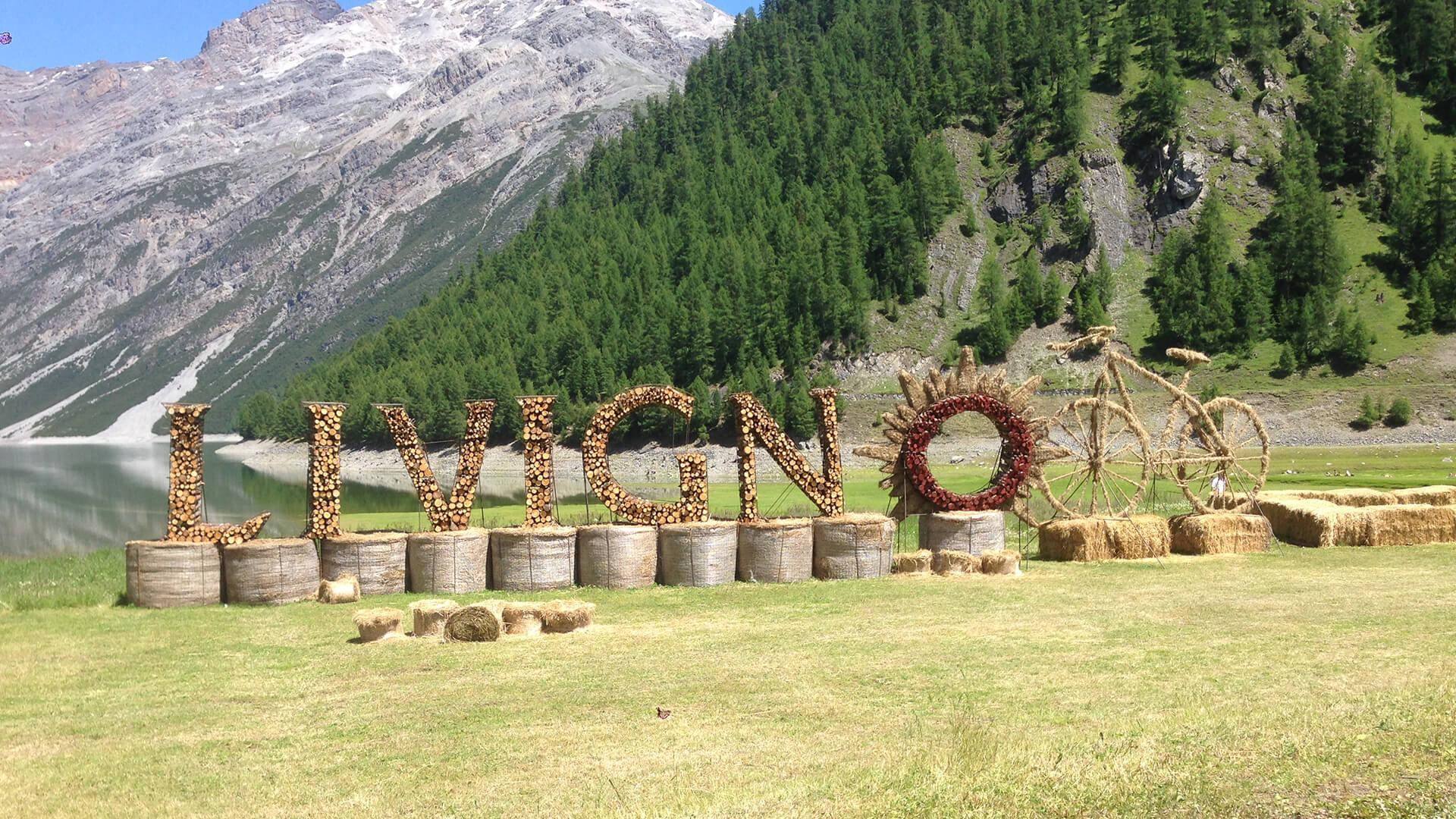 La grande scritta Livigno sul prato in estate, con i boschi e le montagne